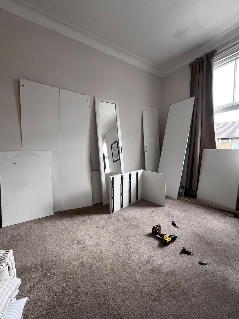 Flat-pack wardrobe panels stacked against a bedroom wall before assembly