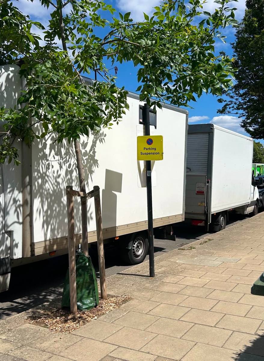 A council parking bay suspension notice beside two Fastiya Logistics removals vans